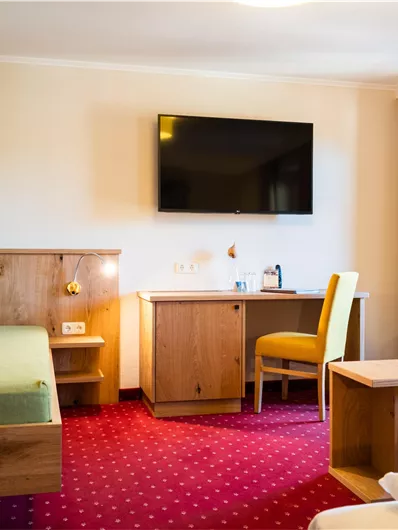 Ein modernes Hotelzimmer mit einem gemütlichen Sofa, einem Tisch und einem Fernseher an der Wand. Der Raum ist gut beleuchtet und hat ein Fenster mit Blick nach draußen.