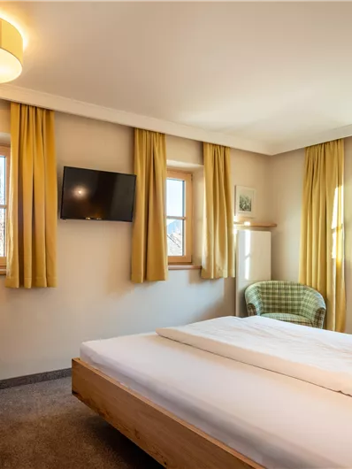 Ein helles Zimmer mit zwei Betten und großen Fenstern. Es gibt einen Schreibtisch, einen Stuhl und eine gemütliche Sitzecke.