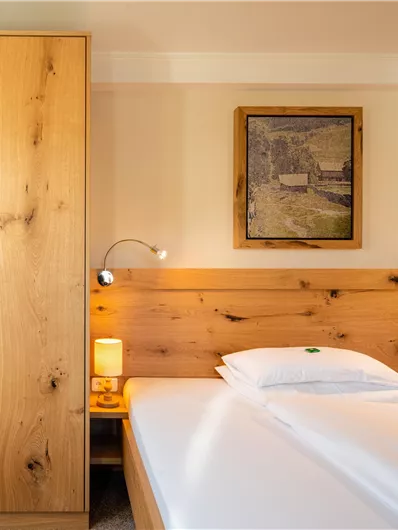 Ein gemütliches Schlafzimmer mit einem Holzbett und einer Kommode. An der Wand hängt ein Bild, und es gibt angenehmes Licht von zwei Nachttischlampen.