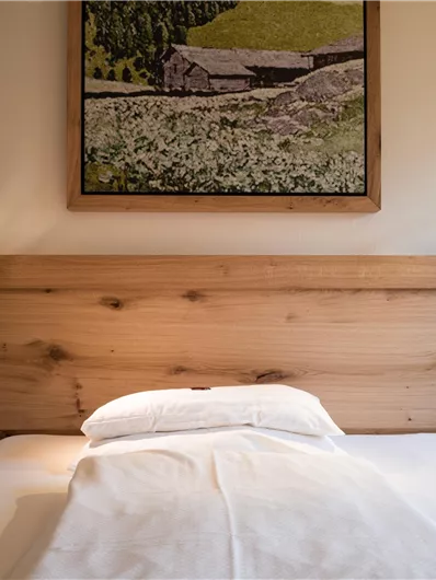 Ein einfaches Schlafzimmer mit einem Holzbett und einem Kunstwerk an der Wand. Es gibt zwei Nachttischlampen und ein sauberes Bett.