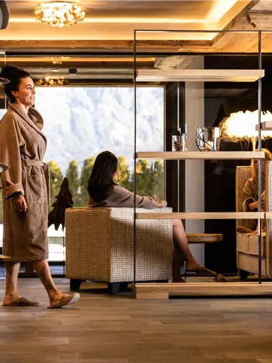 Een elegante spa-lobby met moderne meubels en aangenaam licht. Een vrouw in een badjas loopt ontspannen voorbij, terwijl een andere vrouw zit en de rust geniet.