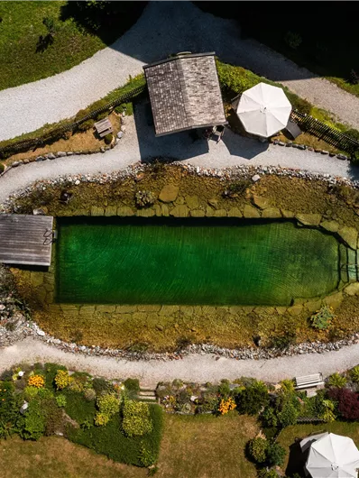 Ein schöner Garten mit einem kleinen, grünen Teich. Umgeben von Wegen, Blumenbeeten und Pavillons ist es ein ruhiger Rückzugsort.