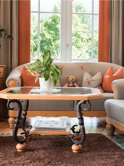 Ein gemütliches Wohnzimmer mit einem runden Tisch und bequemen Sofas. Eine Pflanze und Dekorationen schaffen eine einladende Atmosphäre.