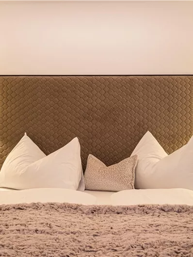 Ein gemütliches Schlafzimmer mit einem großen Bett und weichen Kissen. Ambientebeleuchtung neben dem Bett sorgt für eine entspannende Atmosphäre.
