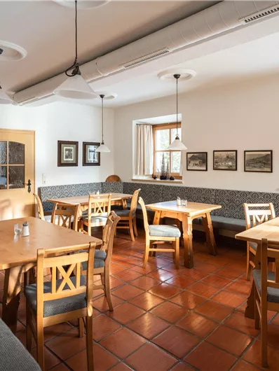 Ein gemütliches Restaurant mit Holztischen und -stühlen. Die Wände sind mit Bildern dekoriert und das Licht ist warm und einladend.