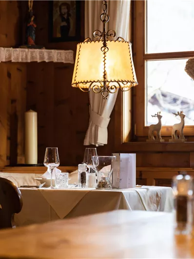 Ein gemütliches Restaurant mit Holzwänden und einem großen Fenster. Auf den Tischen stehen Gläser und Besteck, die Stimmung ist einladend und warm.