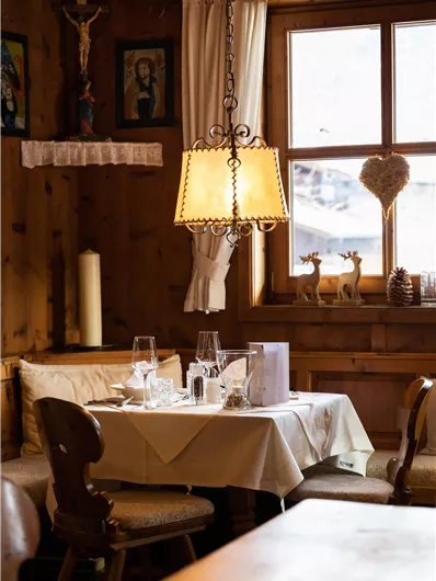 Ein gemütlicher Essbereich in einem rustikalen Restaurant. Der Tisch ist schön gedeckt und eine warm leuchtende Lampe sorgt für eine einladende Atmosphäre.
