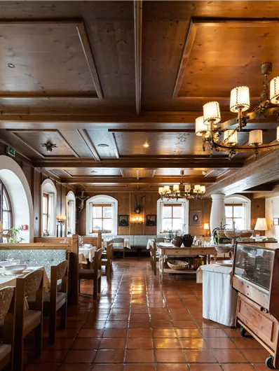 Ein gemütliches Restaurant mit Holzinterieur und warmem Licht. Die Tische sind für Gäste eingedeckt und große Fenster sorgen für eine einladende Atmosphäre.