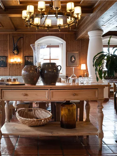 Ein gemütliches Restaurant mit rustikalem Holzdekor und warmem Licht. Tische sind gedeckt und im Hintergrund sind Pflanzen und eine dekorative Einrichtung zu sehen.