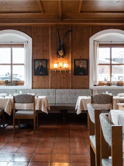 Ein gemütliches Restaurant mit Holzverkleidung und eleganten Tischen. Es gibt große Fenster, die viel Licht hereinlassen, und einige dekorative Elemente an den Wänden.