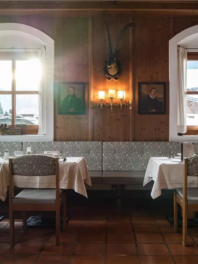 Ein gemütliches Restaurant mit Holzwänden und Fenstern, durch die Licht strömt. Es gibt Tischdecken und gut gedeckte Tische.