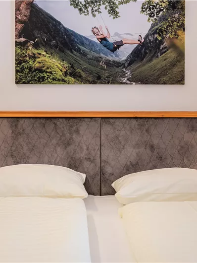Ein gemütliches Schlafzimmer mit einem Doppelbett und sanften, neutralen Farben. Über dem Bett hängt ein großes Bild einer Naturlandschaft.