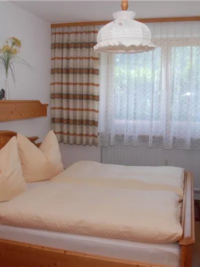 Ein gemütliches Schlafzimmer mit einem Doppelbett und Holzdekor. Große Fenster lassen viel Licht herein und schaffen eine einladende Atmosphäre.