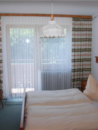 Ein gemütliches Schlafzimmer mit einem Doppelbett und zwei Kissen. Große Fenster bieten viel Licht und einen Blick nach draußen.