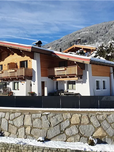 A modern house in alpine style, surrounded by snow. In the background, snow-covered mountains and a blue sky can be seen.