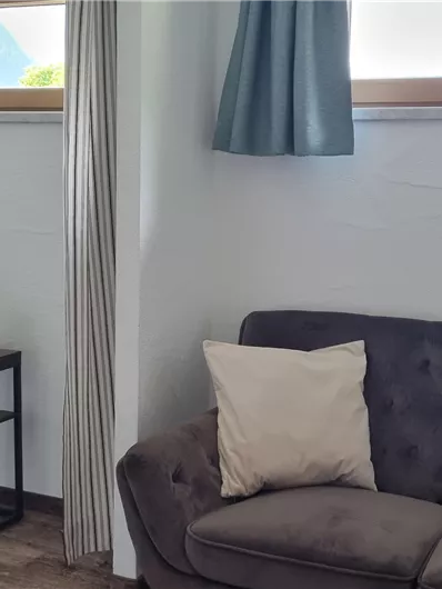 A modern living room with a cozy couch and a small side table. The room features bright curtains and a blooming plant.