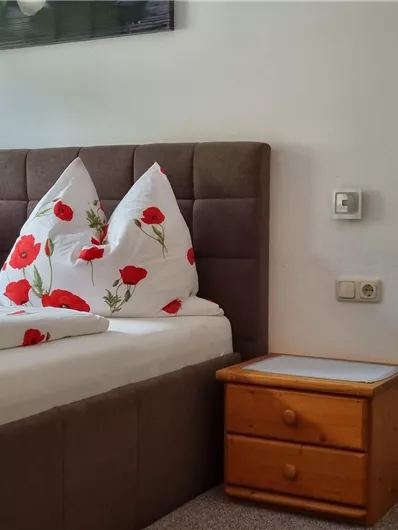 A cozy bedroom with two beds and red pillows. A picture hangs on the wall and there is a wooden nightstand.