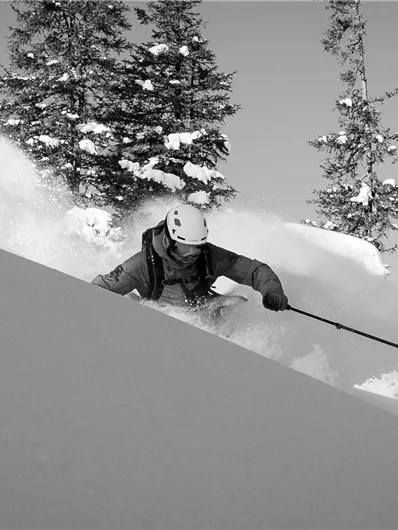 A skier is skiing through fresh, deep snow in a wooded area. The scene is presented in black and white.