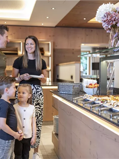 A family is standing at a buffet with various dishes. They are smiling and enjoying their time together.