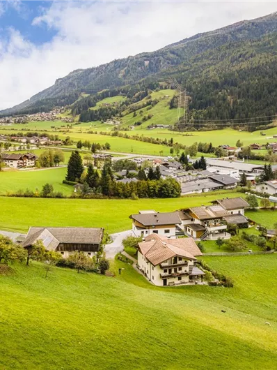 A picturesque landscape with green meadows and gentle hills. Small houses are nestled in nature under a cloudy sky.