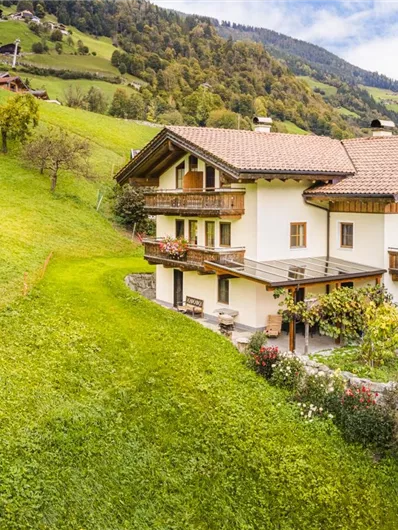An idyllic farmhouse in a green meadow landscape. In the background, gentle hills and cows can be seen.
