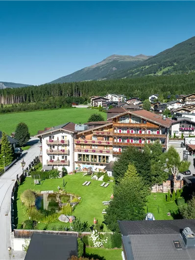 Een schilderachtig bergdorp met een groot hotel en groene weiden. De omgeving is omringd door bosbomen en bergen, ideaal voor natuurliefhebbers.