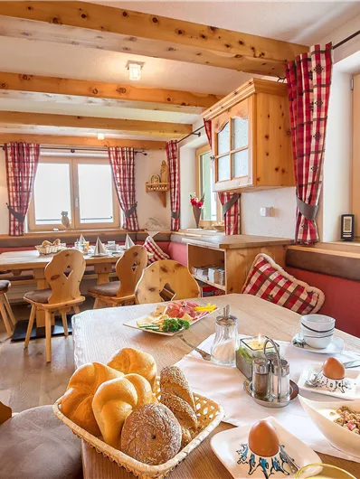 A cozy restaurant with wooden decor and large windows. The table is nicely set with rolls, eggs, and drinks.