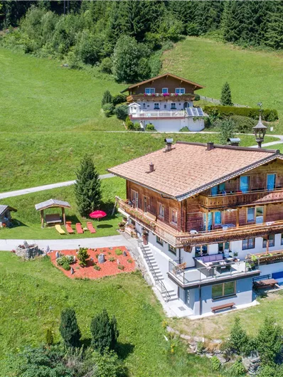 A picturesque mountain landscape with two traditional wooden chalets. Surrounded by green meadows and trees.