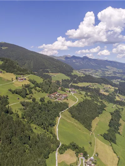 A picturesque landscape with green meadows and gentle hills. In the background, mountains and a blue sky with white clouds are visible.
