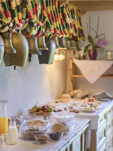 A decorated table with a selection of food and drinks. In the background, large bells hang with colorful ribbons.