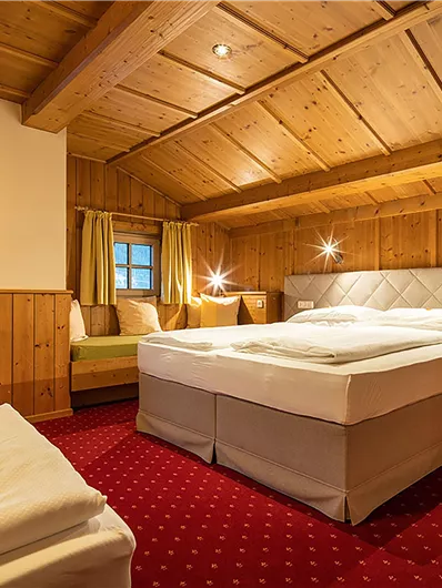 Ein gemütliches Zimmer mit einem Doppelbett und Holzdecken. Es gibt auch eine Sitzecke mit Fenstern, die viel Licht hereinlassen.