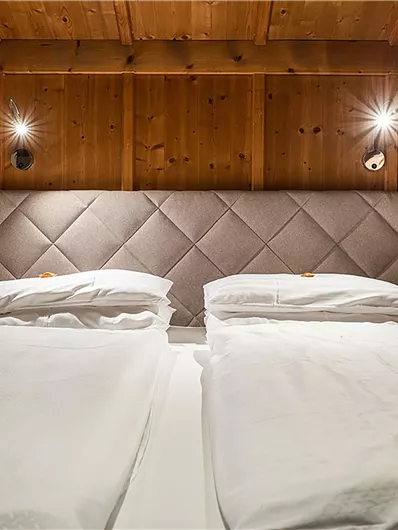 Ein gemütliches Schlafzimmer mit zwei Einzelbetten und einer modernen Kopfteilwand. Die Wände sind mit Holz verkleidet und es gibt stilvolle Wandleuchten.