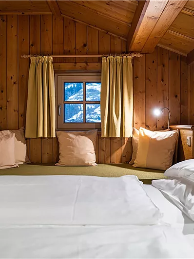 Ein gemütliches Schlafzimmer mit Holzverkleidung und einem Fenster mit Blick auf die Berge. Die Bettwäsche ist weiß und die Atmosphäre ist einladend und warm.