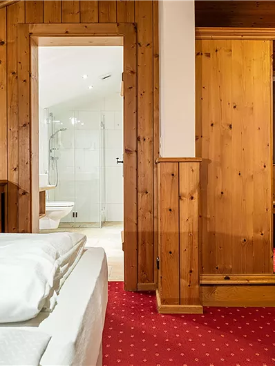 Ein gemütliches Zimmer mit Holzwänden und rotem Teppich. Im Hintergrund ist ein Badezimmer sichtbar.