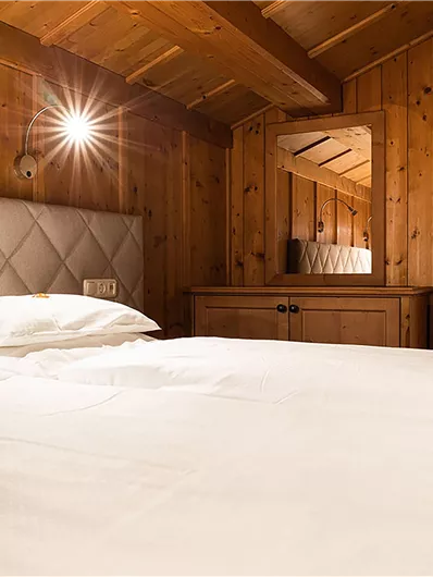 Ein gemütliches Schlafzimmer mit Holzdecke und einem großen Bett. Im Hintergrund sind ein Spiegel und eine Tür zum Badezimmer zu sehen.