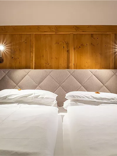 Ein gemütliches Schlafzimmer mit zwei Einzelbetten und einer Holzvertäfelung an der Wand. Die warmen Lichter schaffen eine einladende Atmosphäre.