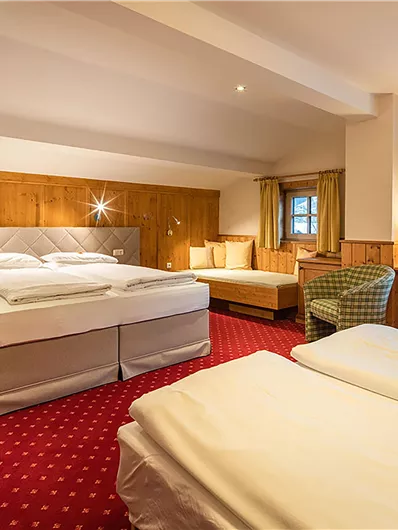 Ein komfortables Hotelzimmer mit zwei Betten und einer gemütlichen Sitzecke. Die warme Holzdecke und die roten Teppiche schaffen eine einladende Atmosphäre.