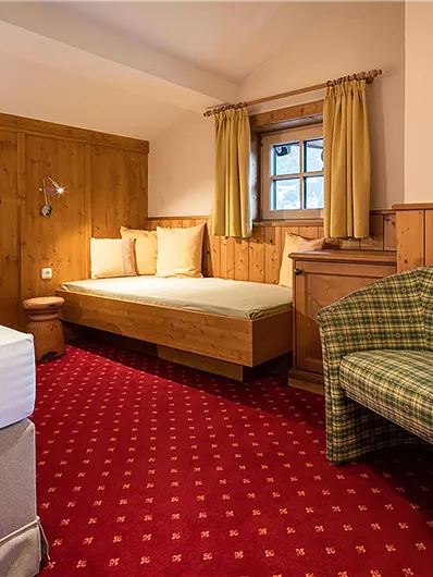 Ein gemütliches Schlafzimmer mit Holzverkleidung und rotem Teppich. Die Ausstattung umfasst ein Bett, einen Sessel und einen Schreibtisch.