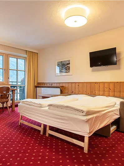 Ein gemütliches Hotelzimmer mit einem großen Bett und Holz-Möbeln. Der Raum hat Fenster mit Blick nach draußen und einen Fernseher an der Wand.
