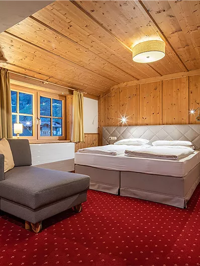 Ein gemütliches Hotelzimmer mit Holzwänden und rotem Teppich. Es verfügt über ein Doppelbett, einen Sitzbereich und große Fenster.