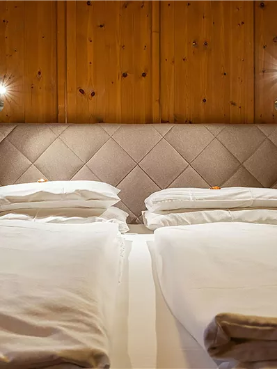 Ein gemütliches Schlafzimmer mit zwei Einzelbetten und einer stilvollen, gepolsterten Kopfteilwand. Die Wände sind aus Holz, was eine warme Atmosphäre schafft.