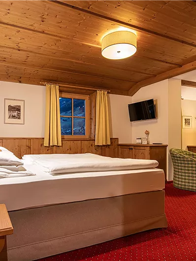 Ein gemütliches Hotelzimmer mit Holzdecken und rotem Teppich. Es verfügt über ein Doppelbett, einen Fernseher und einen gemütlichen Sitzbereich.