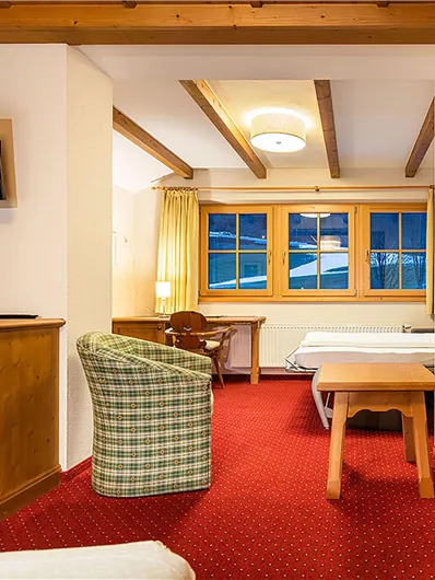 Ein gemütliches Zimmer mit Holzverkleidung und einem Fernseher an der Wand. Es gibt einen Schreibtisch, einen Tisch und ein Fenster mit Blick nach außen.
