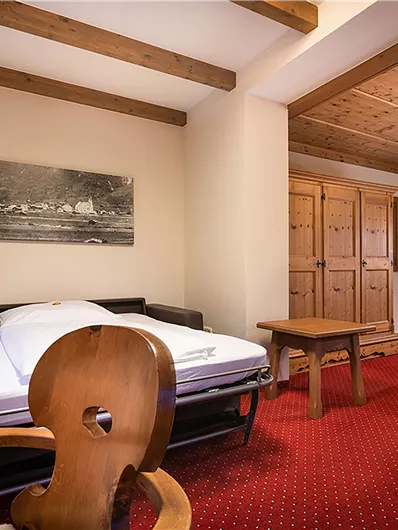 Ein gemütliches Zimmer mit einem Doppelbett und einem Schlafsofa. Die Einrichtung ist rustikal mit Holzdetails und einem bequemen Sessel.