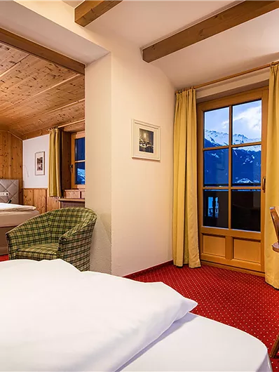 Ein gemütliches Hotelzimmer mit modernem Design. Es gibt ein Bett, einen Schreibtisch und große Fenster mit Blick auf die Berge.