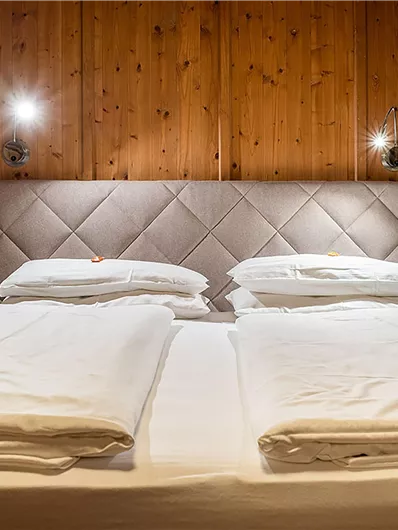 Ein gemütliches Schlafzimmer mit einem großen Doppelbett und Holzverkleidung. Die Nachtlampen an der Wand schaffen eine einladende Atmosphäre.