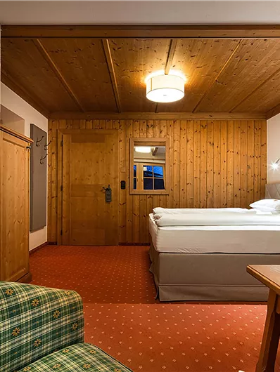 Ein gemütliches Hotelzimmer mit Holzwänden und einem großen Bett. Im Vordergrund steht ein Tisch und eine bequeme Couch.