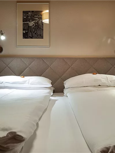 Ein schlichtes Schlafzimmer mit zwei Einzelbetten und warmem Licht. An der Wand hängt ein Kunstwerk und die Atmosphäre ist einladend.