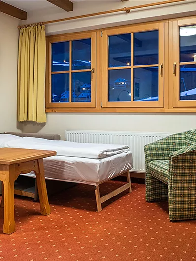 Ein gemütliches Zimmer mit einem Sofa, einem Tisch und einem Stuhl. Große Fenster bieten Blick auf die Umgebung.