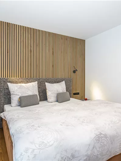 Een moderne slaapkamer met een tweepersoonsbed en een houten lattenwand. De meubels zijn eenvoudig en elegant, met warme houttinten.